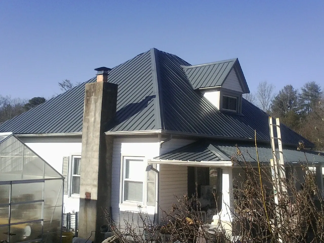 Dark blue standing seam metal roof on a white farmhouse with dormer — Slate & Tile Roof Repair by Roofing Brothers in Shreveport