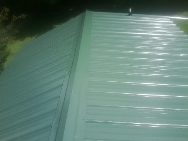 New green metal panels meeting at the ridge of a roof — Flat Roof Repair work by our crew in Shreveport