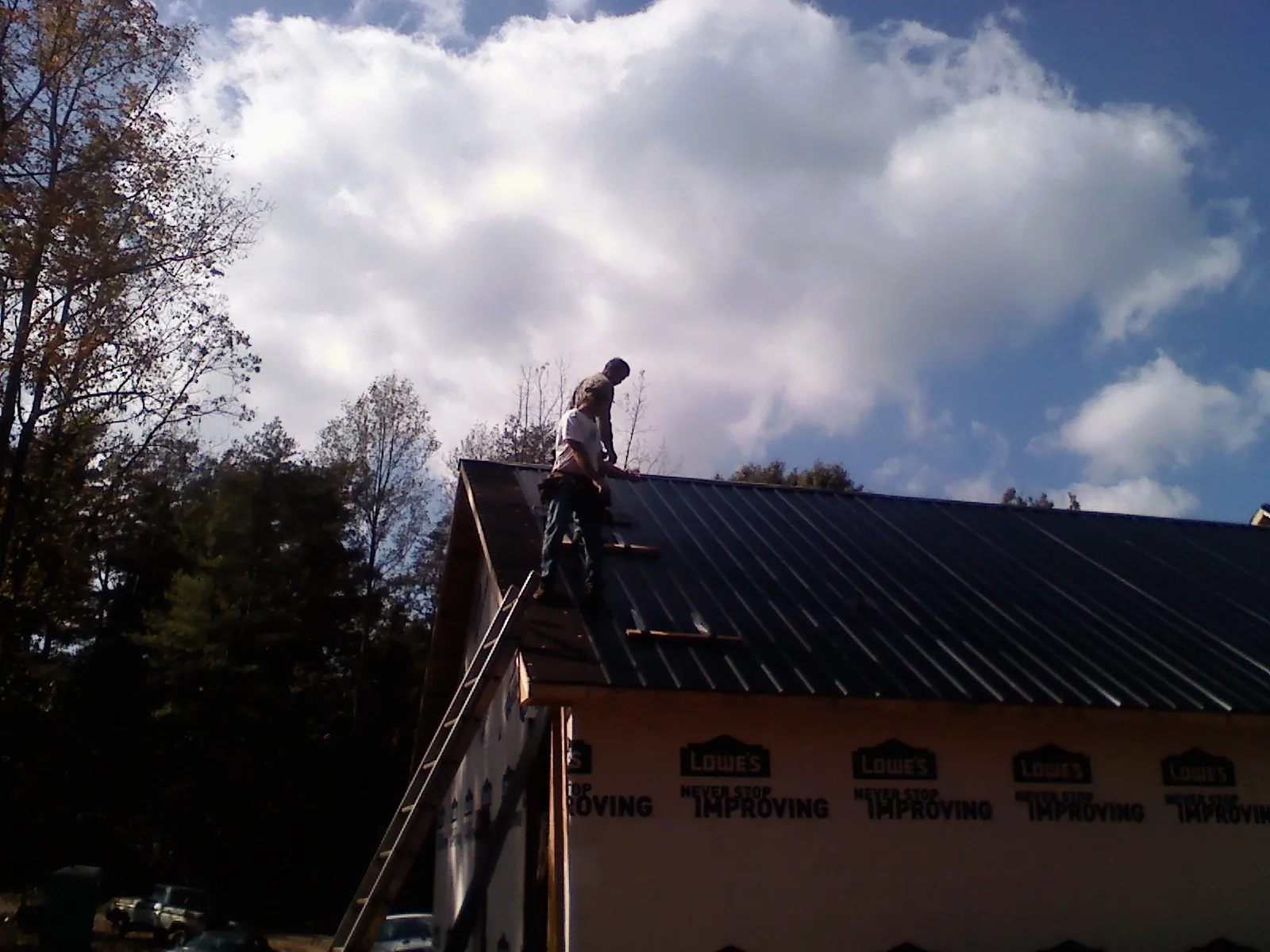 Roofer fastening dark metal panels high against a cloudy sky in Shreveport