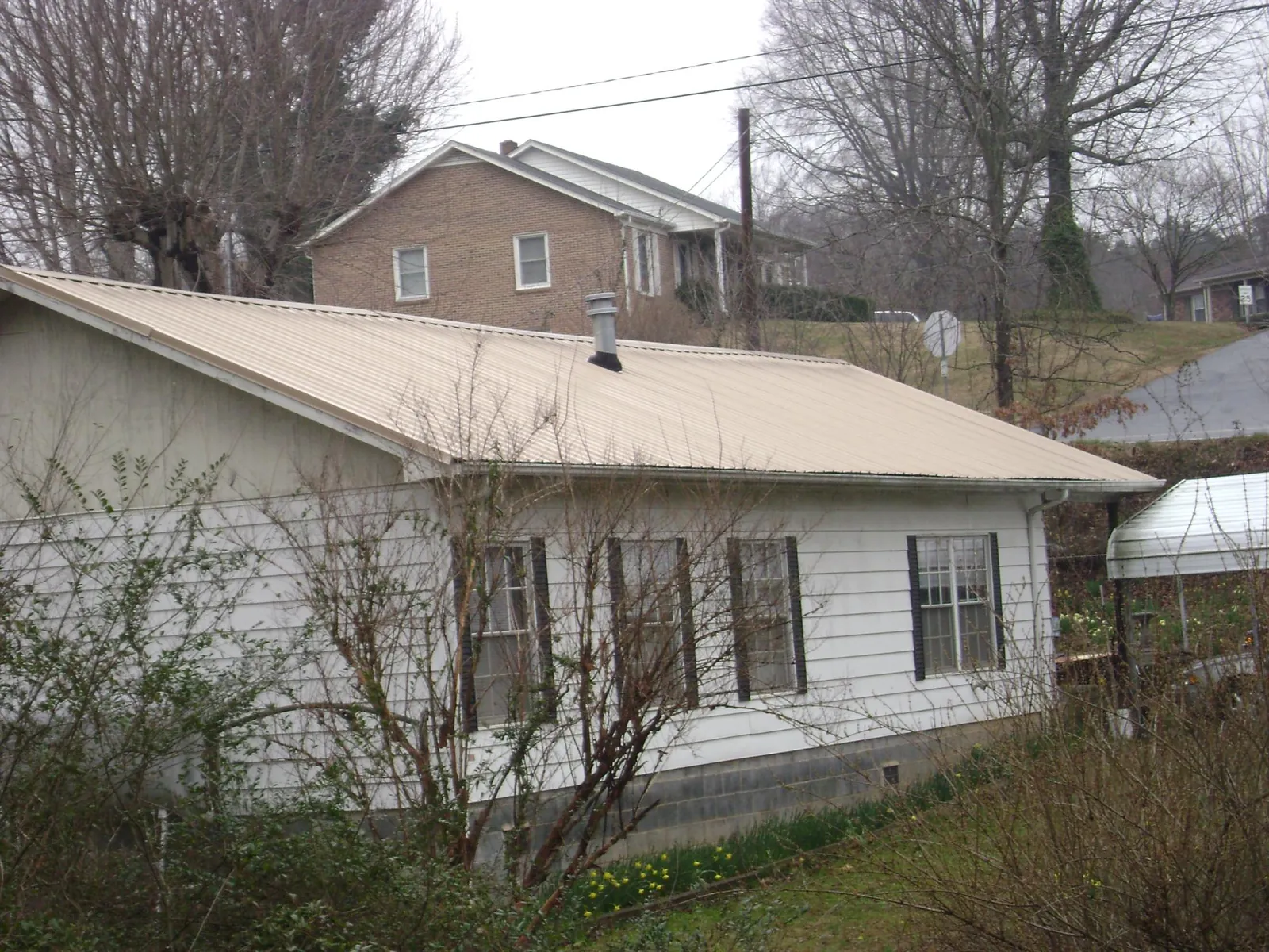 Tan metal roof on a white sided house set into a hillside — Commercial Roofing by Roofing Brothers in Shreveport