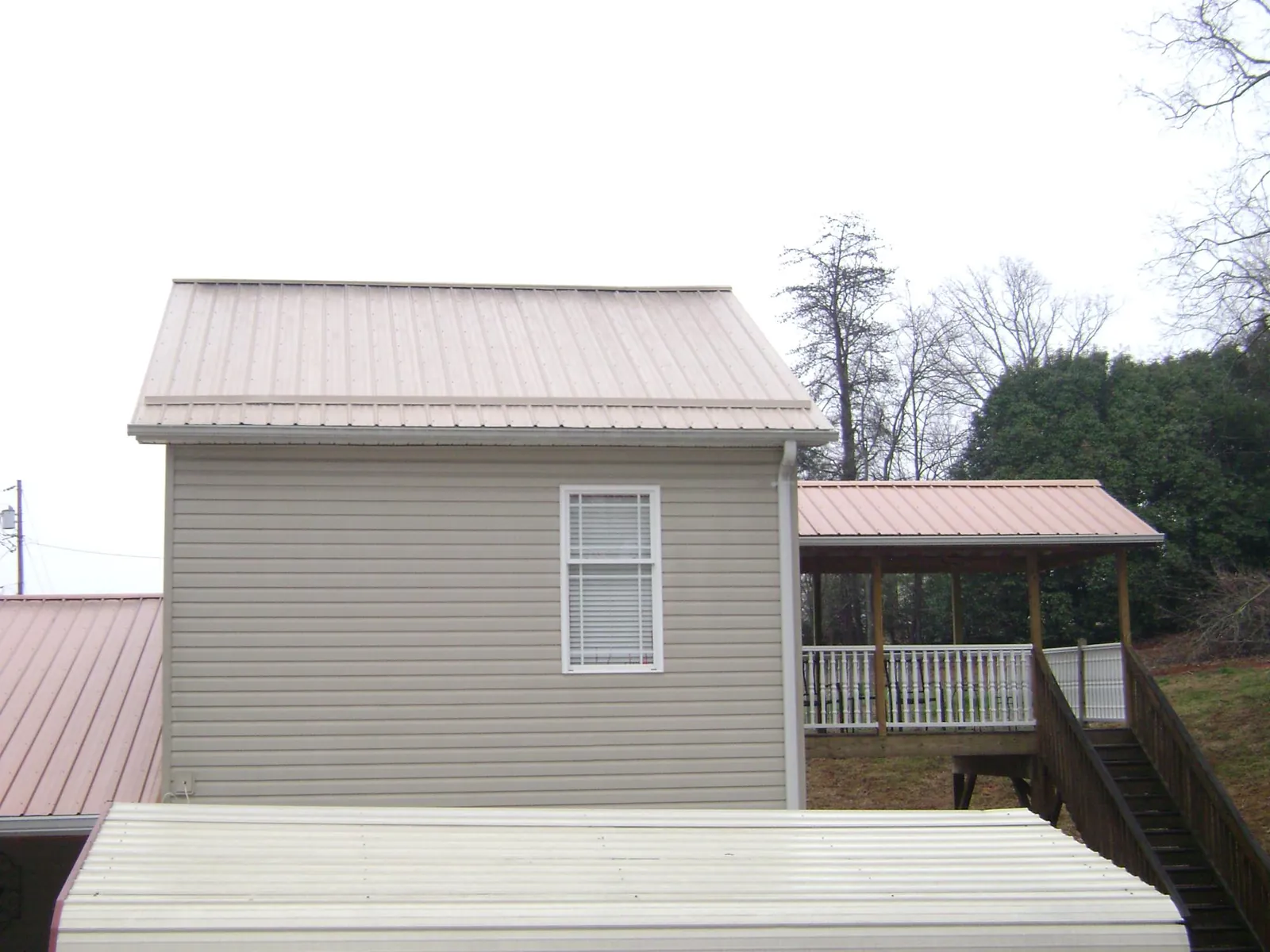 Tan metal roofs on a two story addition and attached porch, from a Roof Replacement job in Shreveport